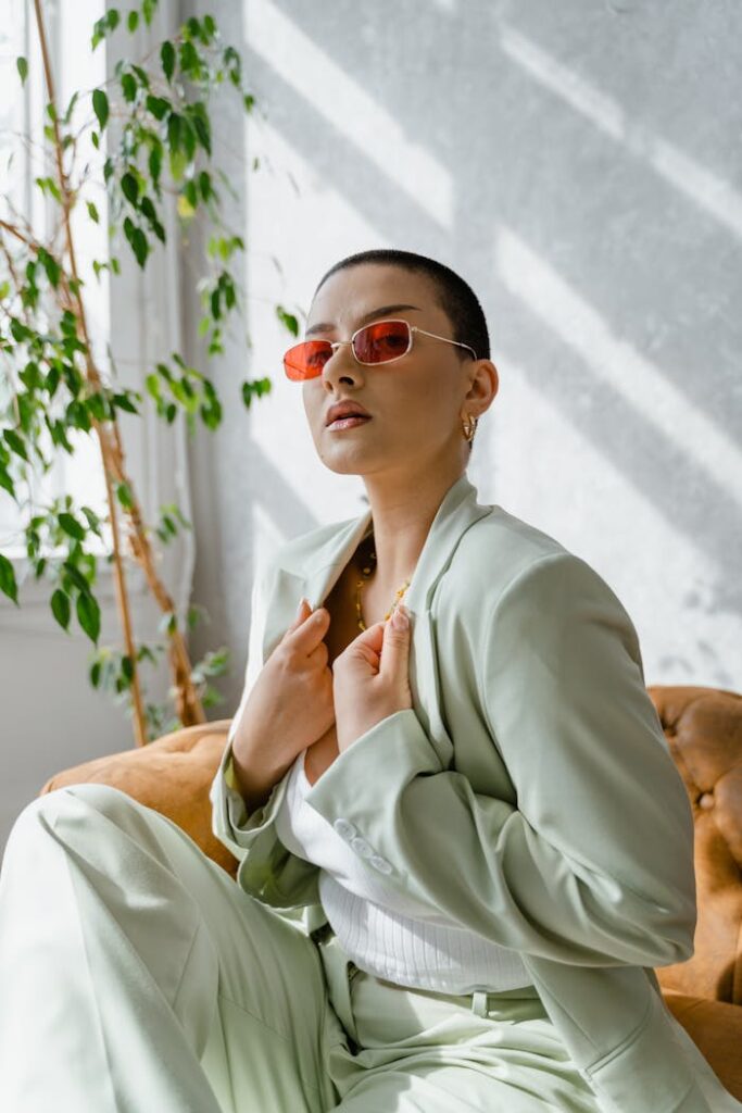 Fashionable woman in a mint green suit with red sunglasses sitting indoors, exuding confidence.